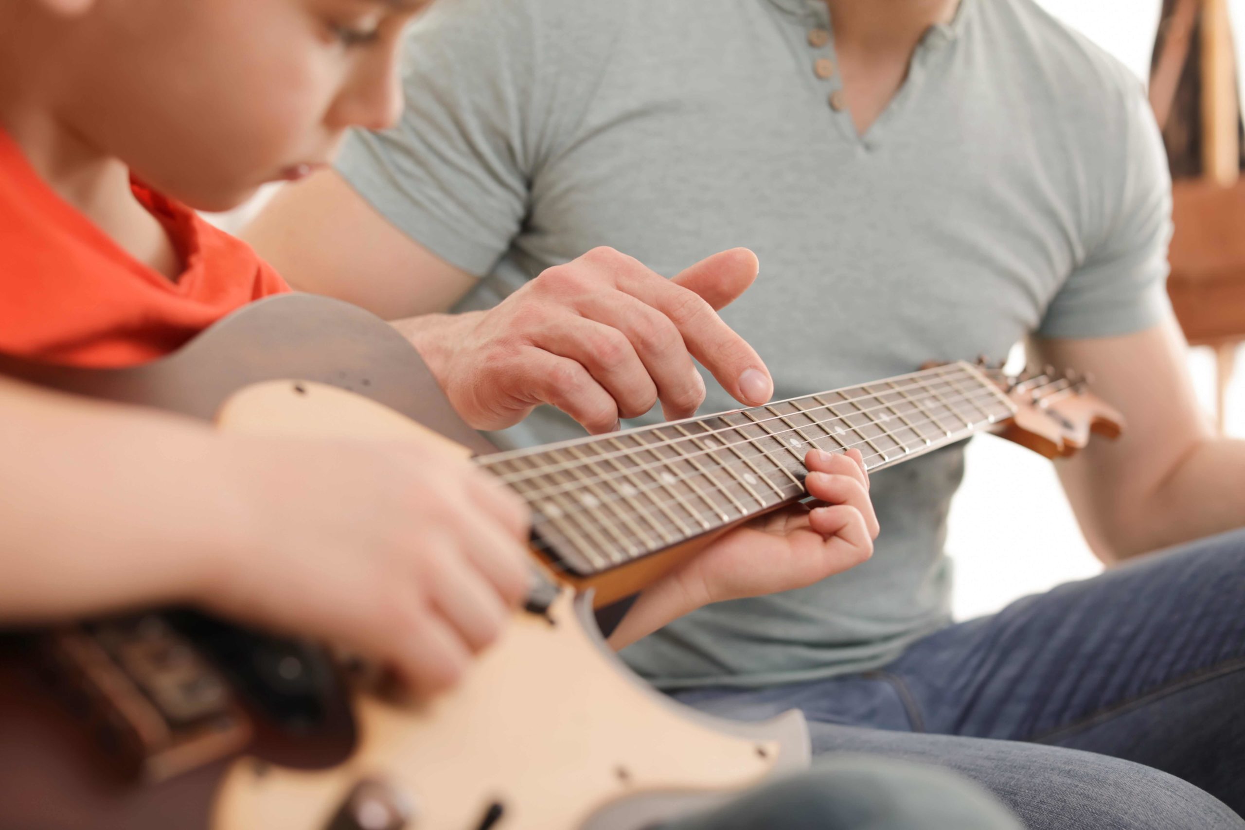 A kid learning guitar from a man